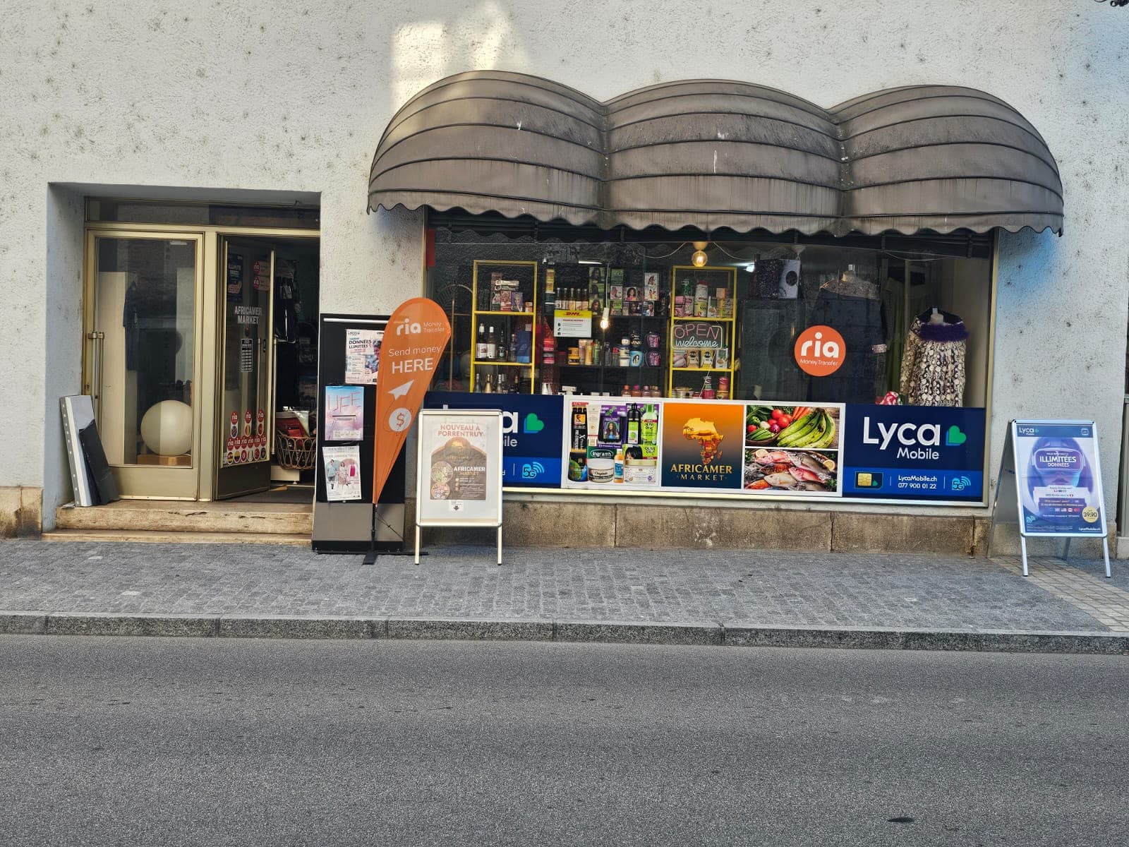 La devanture du magasin, rue piétonne, sous le store, avec les panneaux Ria et Lyca Mobile.
